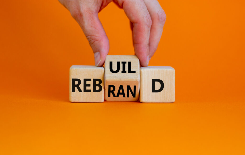 Rebrand and rebuild symbol. Businessman turnsa the wooden cube and changes the word rebrand to rebuild. Beautiful orange table, orange background. Business rebrand and rebuild concept. Copy space.